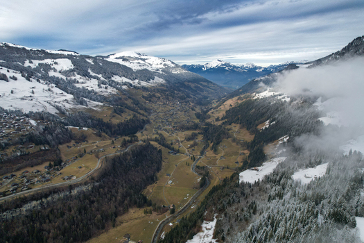 Aerial view of Val d Illiez valley with snow covered mountain peaks dense pine forests and winding roads under a cloudy winter sky in Champery Valais Switzerland.