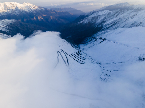 Aerial view of the winding road of Babusar Pass through snow covered mountain peaks and thick white clouds in Babusar KPK Pakistan.