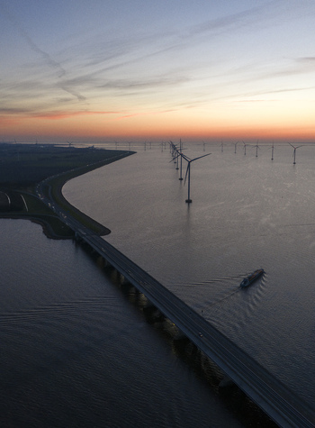 Aerial view of Ketelbrug bridge spanning the water with offshore wind turbines and a cargo ship at sunset Nagele Flevoland Netherlands.