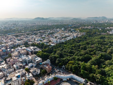 Aerial view of the sprawling urban landscape of Udaipur featuring dense green foliage residential rooftops and distant hills in Udaipur Rajasthan India.