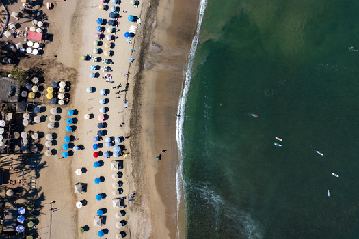 Aerial view of colorful beach umbrellas lining the sandy shore with people swimming and surfing in the clear turquoise water Sayulita Nayarit Mexico. Aerial view of colorful beach umbrellas lining the sandy shore with people swimming and surfing in the clear turquoise water Sayulita Nayarit Mexico.