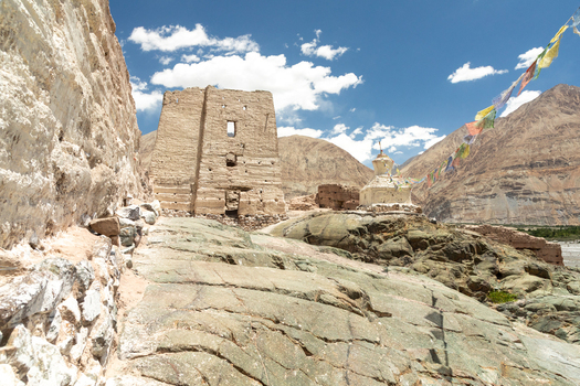 View of Charasa Gonpa an ancient Buddhist monastery with weathered stone walls and a stupa set against a rugged mountain landscape under a blue sky in Charasa Ladakh India.