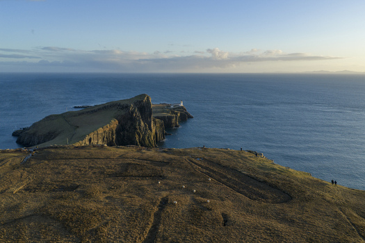 Aerial view of Neist Point Lighthouse on the edge of dramatic cliffs overlooking the blue sea with sheep grazing on the grassy hills Isle of Skye Scotland United Kingdom. Aerial view of Neist Point Lighthouse on the edge of dramatic cliffs overlooking the blue sea with sheep grazing on the grassy hills Isle of Skye Scotland United Kingdom.