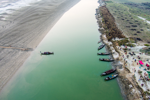 Aerial view of traditional wooden boats moored along the sandy banks of the Padma River with people walking nearby in Rajshahi Rajshahi Division Bangladesh.