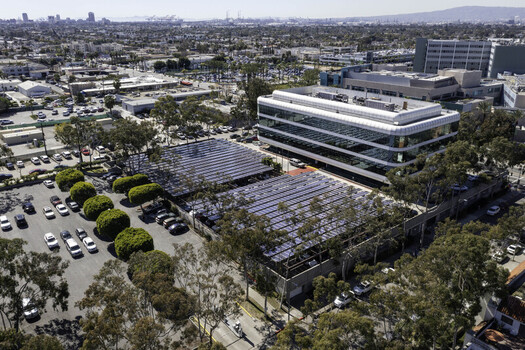 Aerial view of a large solar array covering a parking lot next to a modern office building in Los Angeles California United States. Aerial view of a large solar array covering a parking lot next to a modern office building in Los Angeles California United States.