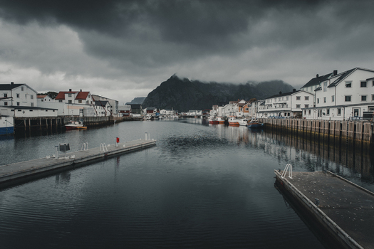 View of the harbor in Henningsvaer with traditional white houses wooden piers and fishing boats under a dramatic cloudy sky in Henningsvaer Nordland Norway. View of the harbor in Henningsvaer with traditional white houses wooden piers and fishing boats under a dramatic cloudy sky in Henningsvaer Nordland Norway.