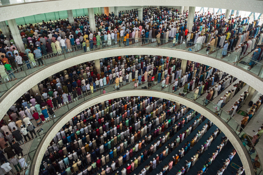 Dhaka Bangladesh 19 June 2026 Aerial view of a large crowd of men praying inside a modern mosque with curved balconies and bright interior lighting.
