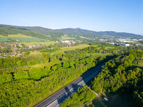 Aerial view of Liberec D10 highway winding through lush green forests and rolling hills under a clear blue sky in Liberec Liberec Region Czechia.