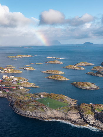 Aerial view of the iconic soccer field on a rocky island in the Lofoten archipelago with scattered houses deep blue sea and a rainbow in the sky in Leknes Nordland Norway. Aerial view of the iconic soccer field on a rocky island in the Lofoten archipelago with scattered houses deep blue sea and a rainbow in the sky in Leknes Nordland Norway.