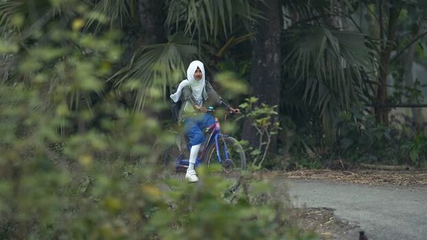 View of a schoolgirl riding a bicycle on a rural road Bangladesh. View of a schoolgirl riding a bicycle on a rural road Bangladesh.