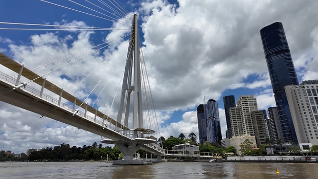 View of the Kurilpa Bridge spanning the Brisbane River with modern skyscrapers in the background under a blue sky with clouds in Brisbane Queensland Australia. View of the Kurilpa Bridge spanning the Brisbane River with modern skyscrapers in the background under a blue sky with clouds in Brisbane Queensland Australia.