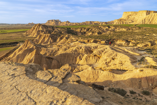 View of the Bardenas Reales badlands with a person in a red jacket standing among eroded clay formations and sandstone plateaus in Navarre Spain. View of the Bardenas Reales badlands with a person in a red jacket standing among eroded clay formations and sandstone plateaus in Navarre Spain.