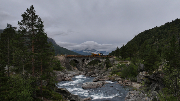 Aerial view of a stone arch bridge spanning a rushing river in a mountainous landscape with construction machinery on the bridge in Nordland Norway. Aerial view of a stone arch bridge spanning a rushing river in a mountainous landscape with construction machinery on the bridge in Nordland Norway.