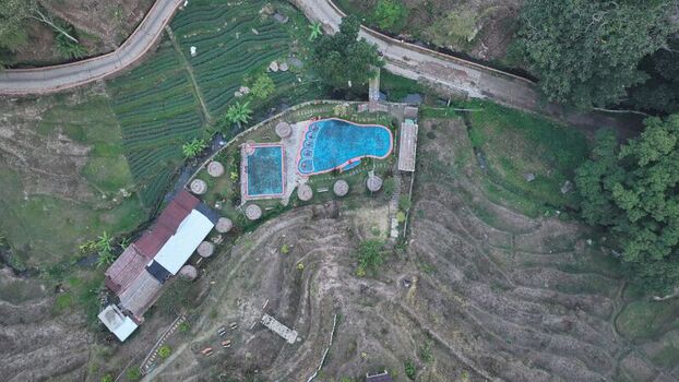 Aerial view of a swimming pool complex nestled among terraced rice fields and lush greenery in Trawas East Java Indonesia. Aerial view of a swimming pool complex nestled among terraced rice fields and lush greenery in Trawas East Java Indonesia.