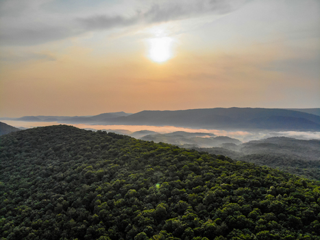 Lost City West Virginia United States 12 June 2019 Aerial view of lush forested hills and valleys filled with morning fog under a soft sunrise sky. Lost City West Virginia United States 12 June 2019 Aerial view of lush forested hills and valleys filled with morning fog under a soft sunrise sky.