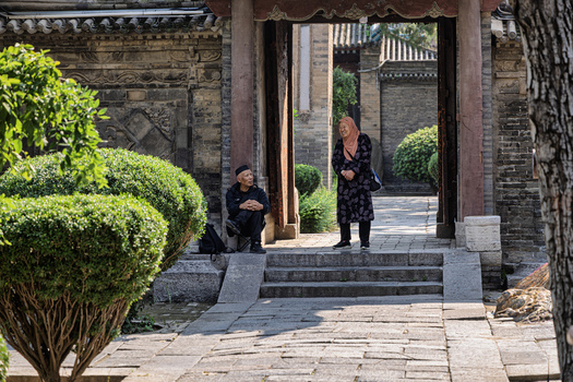 Xi an China 14 September 2026 View of an elderly man sitting and an elderly woman standing in the courtyard of the historic Great Mosque of Xi an with traditional architecture and stone pathways.