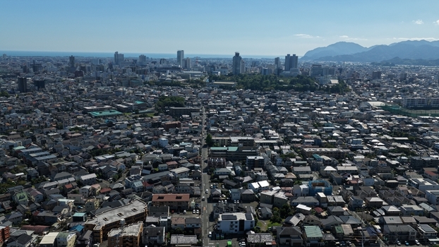 Aerial view of the dense urban landscape of Shizuoka City featuring residential rooftops commercial buildings and the distant Suruga Bay under a clear blue sky in Shizuoka Shizuoka Japan.