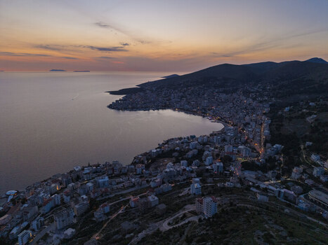 Aerial view of the coastal city of Saranda at sunset featuring urban buildings along the Ionian Sea coastline and hills in Saranda Vlore County Albania. Aerial view of the coastal city of Saranda at sunset featuring urban buildings along the Ionian Sea coastline and hills in Saranda Vlore County Albania.