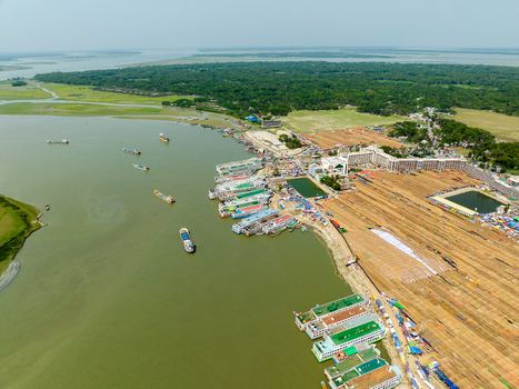 Aerial view of boats lined up along the riverbank reflecting the sky next to a vast flat land filled with rows of what appear to be haystacks Charmonai Bangladesh. Aerial view of boats lined up along the riverbank reflecting the sky next to a vast flat land filled with rows of what appear to be haystacks Charmonai Bangladesh.