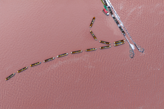 Aerial view of fishing boats cutting through the pink waters of the salt flats contrasting against the stark white of the salt piles San Pedro del Pinatar Region of Murcia Spain. Aerial view of fishing boats cutting through the pink waters of the salt flats contrasting against the stark white of the salt piles San Pedro del Pinatar Region of Murcia Spain.