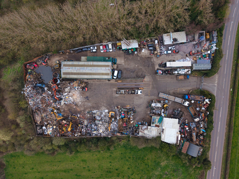 Aerial view of a recycling center where piles of scrap metal and crushed vehicles contrast starkly with the surrounding green fields and roadside Stafford England United Kingdom. Aerial view of a recycling center where piles of scrap metal and crushed vehicles contrast starkly with the surrounding green fields and roadside Stafford England United Kingdom.