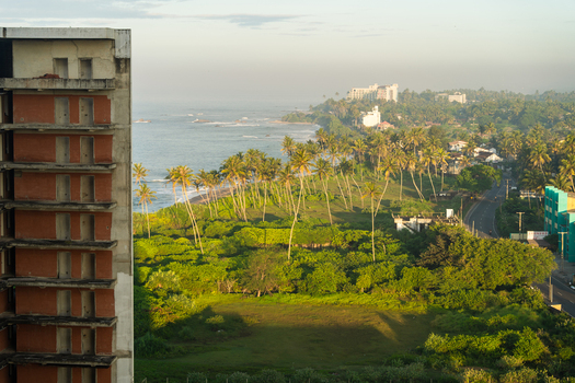 View of the tropical coastline with palm trees an unfinished building and a winding road along the ocean in Galle Southern Province Sri Lanka.