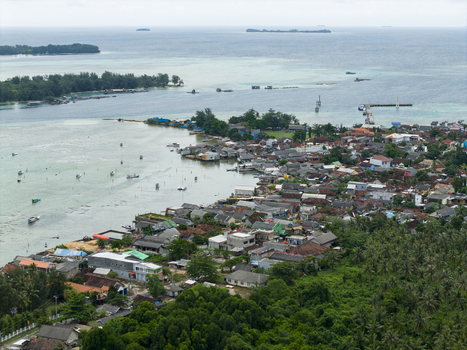 Aerial view of the coastal town with red roofed buildings nestled amidst lush greenery meeting the turquoise sea Karimunjawa Central Java Indonesia. Aerial view of the coastal town with red roofed buildings nestled amidst lush greenery meeting the turquoise sea Karimunjawa Central Java Indonesia.