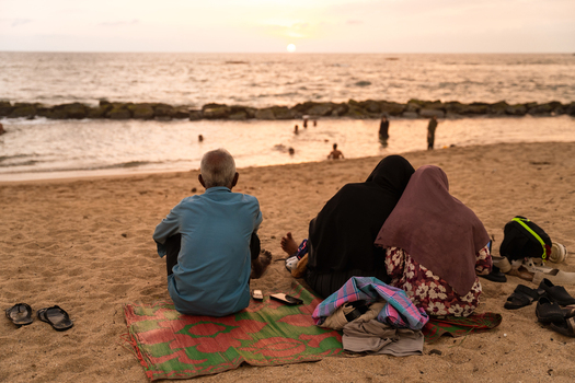 Sri Lanka 14 January 2026 View of a man and two women sitting on the sand watching the sunset over the Indian Ocean with gentle waves and a soft sky.