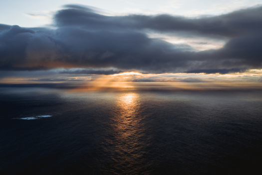 Aerial view of sunbeams piercing through brooding clouds casting a golden glow on the tranquil waters of the Norwegian Sea Henningsv&aelig;r Nordland Norway.