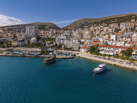 Aerial view of the coastal city of Saranda with boats docked in the harbor urban buildings rising along the hillside and turquoise waters in Saranda Vlore County Albania. Aerial view of the coastal city of Saranda with boats docked in the harbor urban buildings rising along the hillside and turquoise waters in Saranda Vlore County Albania.