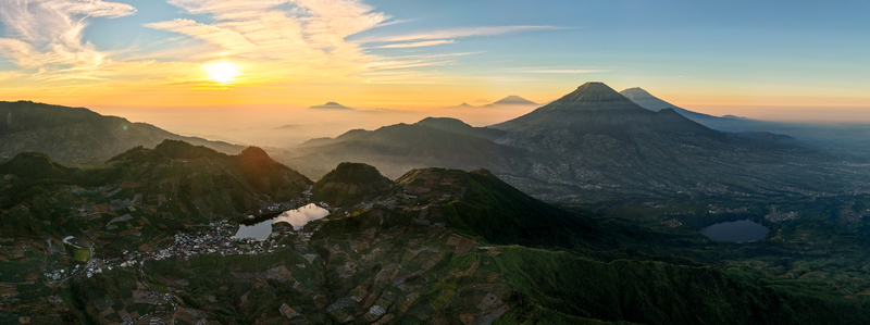 Aerial view of the Dieng Plateau landscape featuring Telaga Cebong lake terraced agricultural fields and the majestic Mount Sindoro at sunrise in Kecamatan Kejajar Jawa Tengah Indonesia.