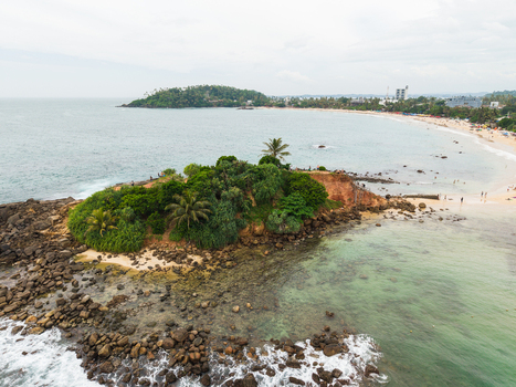 Aerial view of Parrot Rock surrounded by turquoise waters and the sandy coastline with palm trees in Mirissa Southern Province Sri Lanka. Aerial view of Parrot Rock surrounded by turquoise waters and the sandy coastline with palm trees in Mirissa Southern Province Sri Lanka.