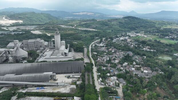 Aerial view of a large cement factory complex situated next to a dense residential neighborhood with lush green hills in the background in Klapanunggal West Java Indonesia. Aerial view of a large cement factory complex situated next to a dense residential neighborhood with lush green hills in the background in Klapanunggal West Java Indonesia.