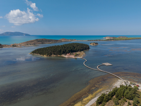 Aerial view of Zvernec Islands featuring the wooden footbridge connecting to the mainland surrounded by the Narta Lagoon clear blue water and lush pine forests in Vlore Vlore County Albania. Aerial view of Zvernec Islands featuring the wooden footbridge connecting to the mainland surrounded by the Narta Lagoon clear blue water and lush pine forests in Vlore Vlore County Albania.