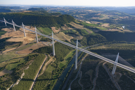 Aerial view of the Millau Viaduct standing tall amidst the valley s verdant tapestry its sleek lines cutting through the landscape Millau France. Aerial view of the Millau Viaduct standing tall amidst the valley s verdant tapestry its sleek lines cutting through the landscape Millau France.