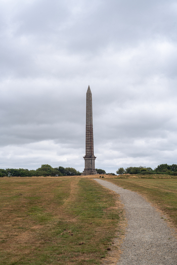View of the Bodmin Beacon stone obelisk monument standing in a grassy field with a gravel path leading towards it under a cloudy sky in Bodmin Cornwall United Kingdom. View of the Bodmin Beacon stone obelisk monument standing in a grassy field with a gravel path leading towards it under a cloudy sky in Bodmin Cornwall United Kingdom.