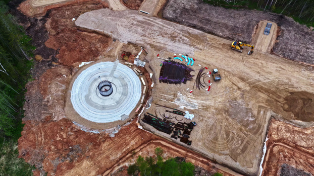 Aerial view of a wind turbine foundation under construction with a circular concrete base heavy machinery and scattered building materials on a dirt site in Latvia. Aerial view of a wind turbine foundation under construction with a circular concrete base heavy machinery and scattered building materials on a dirt site in Latvia.