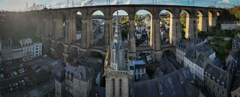 Aerial view of the Eglise Saint Melaine de Morlaix spire and the massive stone arches of the Viaduc de Morlaix overlooking the historic town rooftops in Morlaix Bretagne France. Aerial view of the Eglise Saint Melaine de Morlaix spire and the massive stone arches of the Viaduc de Morlaix overlooking the historic town rooftops in Morlaix Bretagne France.
