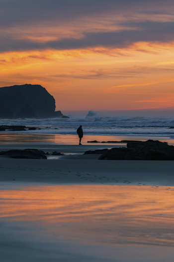 View of a serene sunset at the seashore with a man silhouetted against the ocean Praia da Cordoama Sagres Algarve Portugal.