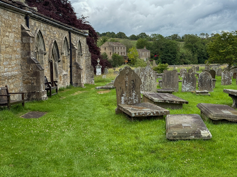 View of a historic stone church and weathered headstones in a green graveyard under a cloudy sky Hawes England United Kingdom. View of a historic stone church and weathered headstones in a green graveyard under a cloudy sky Hawes England United Kingdom.