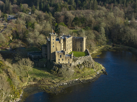 Aerial view of Dunvegan Castle and Gardens on a rocky cliff overlooking the water surrounded by lush green forests Isle of Skye Scotland United Kingdom. Aerial view of Dunvegan Castle and Gardens on a rocky cliff overlooking the water surrounded by lush green forests Isle of Skye Scotland United Kingdom.