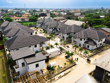 Aerial view of a modern residential complex featuring white houses with dark grey roofs palm trees and a dense urban skyline in Port Harcourt Rivers Nigeria. Aerial view of a modern residential complex featuring white houses with dark grey roofs palm trees and a dense urban skyline in Port Harcourt Rivers Nigeria.
