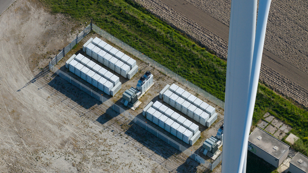 Aerial view of a battery energy storage system with rows of white containers next to a wind turbine mast in Ooltgensplaat Zuid Holland Netherlands. Aerial view of a battery energy storage system with rows of white containers next to a wind turbine mast in Ooltgensplaat Zuid Holland Netherlands.