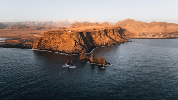 Aerial view of basalt sea stacks of Reynisdrangar rise dramatically from the dark churning ocean waters framed by rugged cliffs Reynisdrangar Iceland.