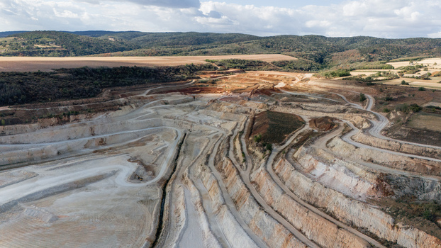 Aerial view of the open pit quarry in Besenovo featuring terraced excavation levels winding access roads and surrounding hilly landscape under a cloudy sky in Besenovo Vojvodina Serbia. Aerial view of the open pit quarry in Besenovo featuring terraced excavation levels winding access roads and surrounding hilly landscape under a cloudy sky in Besenovo Vojvodina Serbia.