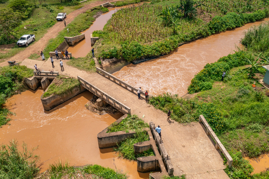 Aerial view of a concrete bridge crossing a muddy river with people standing on the structure and vehicles parked on the dirt road in Butaleja Eastern Region Uganda. Aerial view of a concrete bridge crossing a muddy river with people standing on the structure and vehicles parked on the dirt road in Butaleja Eastern Region Uganda.