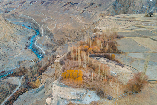Aerial view of a turquoise river snaking through the arid landscape with golden trees clinging to the cliff s edge Hunza Nagar Gilgit Pakistan. Aerial view of a turquoise river snaking through the arid landscape with golden trees clinging to the cliff s edge Hunza Nagar Gilgit Pakistan.