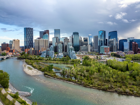 Aerial view of the downtown skyline featuring modern skyscrapers the Bow River and lush green parkland under a cloudy sky in Calgary Alberta Canada.
