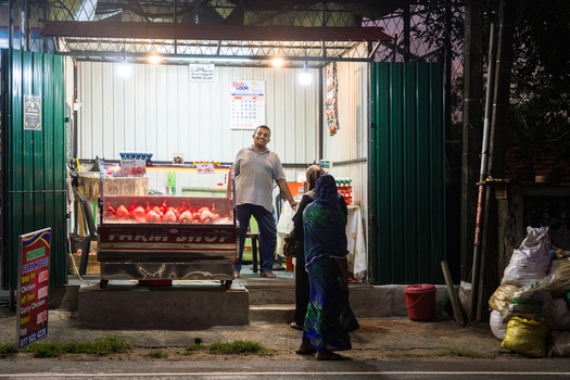 Sri Lanka 14 January 2026 View of a small roadside poultry stall at night with a man standing inside under bright lights and a woman waiting outside.