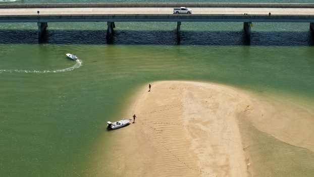 Aerial view of Matanzas Inlet with a bridge spanning the water a small boat anchored on a sandy shoal and people walking on the beach in St. Johns County Florida United States. Aerial view of Matanzas Inlet with a bridge spanning the water a small boat anchored on a sandy shoal and people walking on the beach in St. Johns County Florida United States.